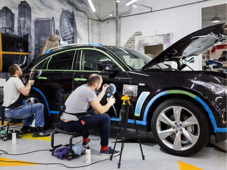 Два майстри полірують чорний автомобіль в сервісному центрі.
