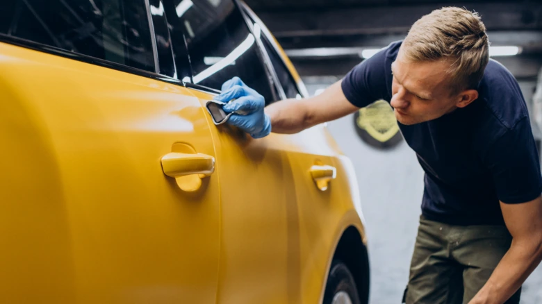 Чоловік у рукавичках полірує жовтий автомобіль.