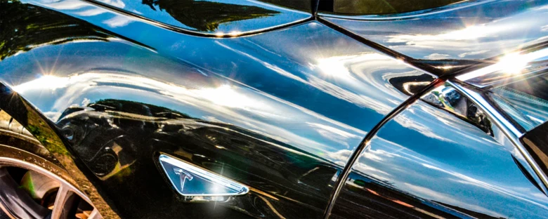 Блещучий капот чорного автомобіля з логотипом Tesla.